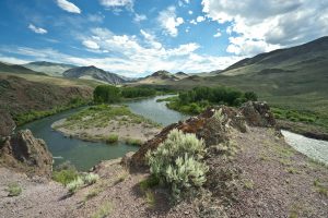 River winding through mountainous landscape under a cloudy blue sky.