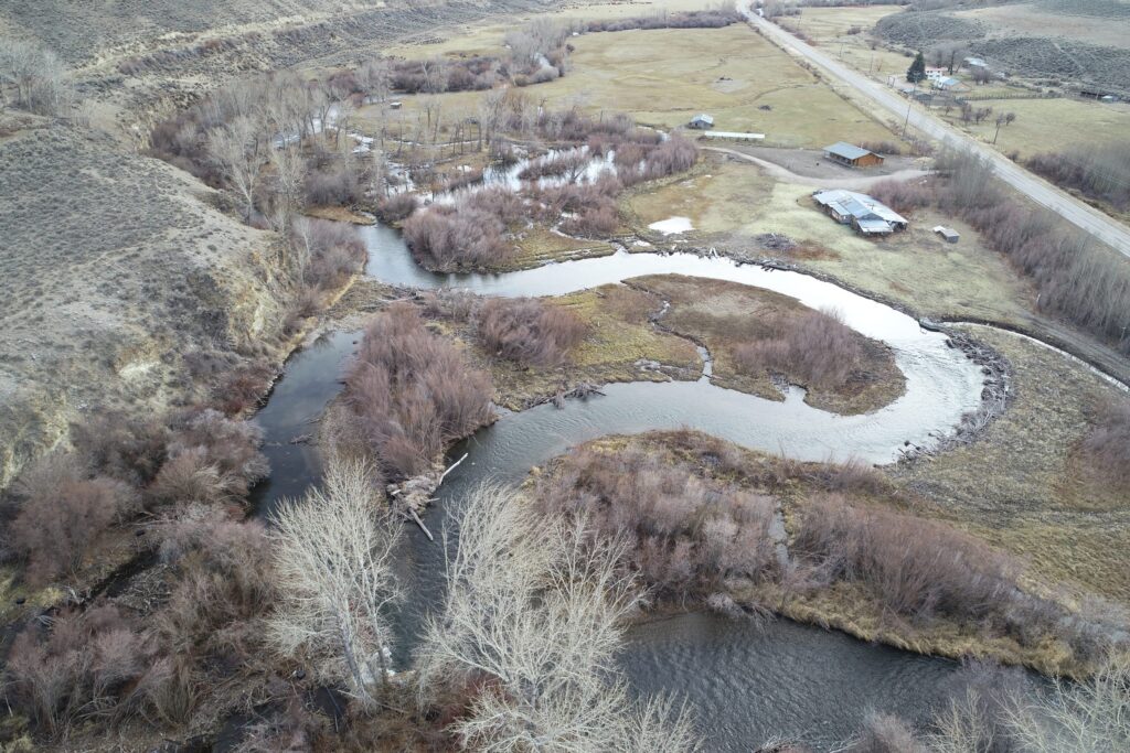 Aerial view of a winding river through grasslands, surrounded by trees and buildings.
