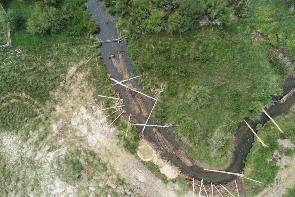Aerial view of a stream, grasslands, and sparse wooden debris or structures.