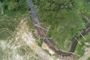 Aerial view of a stream, grasslands, and sparse wooden debris or structures.